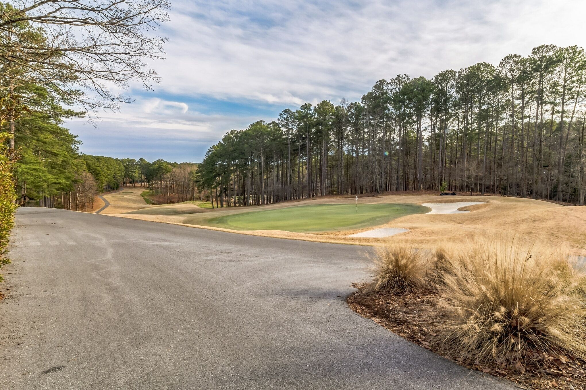 A golf course with a well-maintained fairway, sand bunkers, and a wooded backdrop.