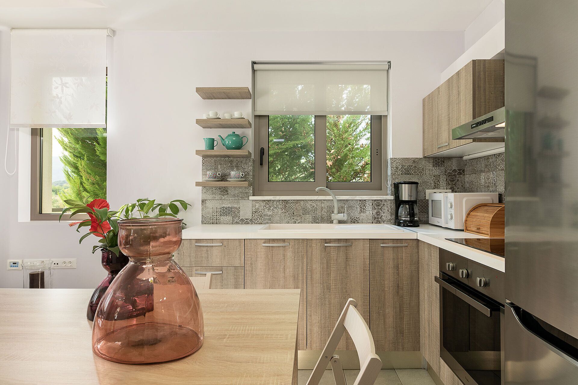 Une cuisine moderne avec des meubles en bois, un réfrigérateur en acier inoxydable, une machine à café et une fenêtre donnant sur la verdure.