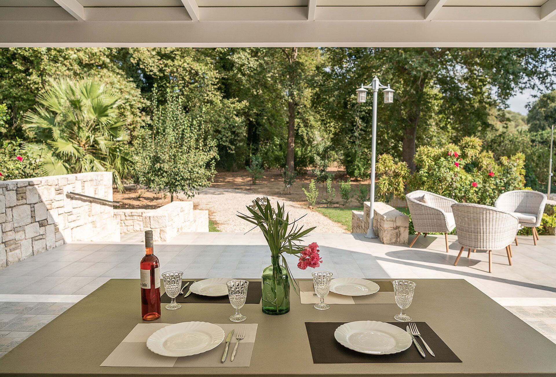 An outdoor dining area with a table set for two, surrounded by stone walls and greenery.
