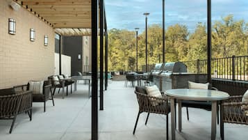 An outdoor patio area with wicker furniture, a round table, and a barbecue grill.