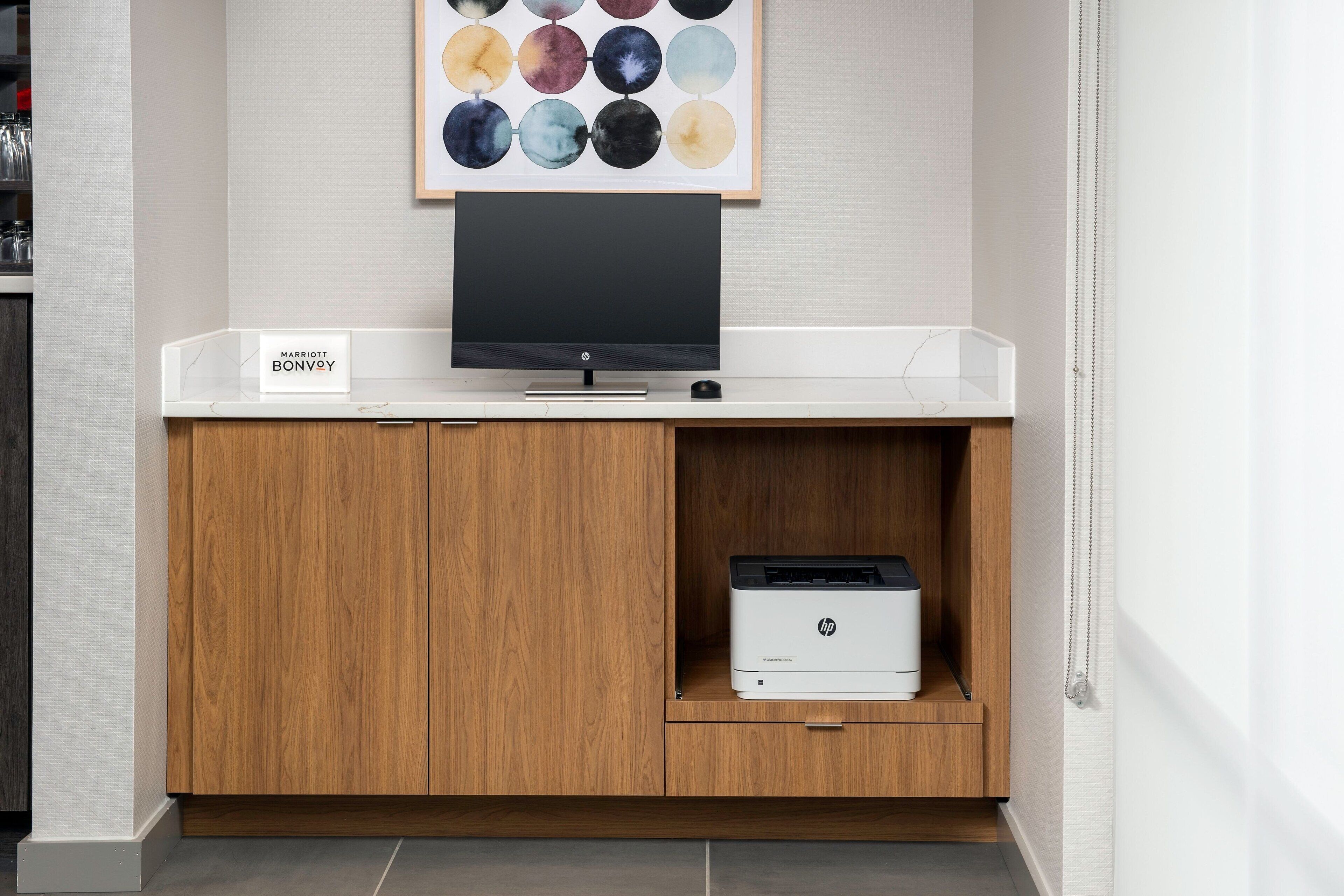 A clean, modern hotel room with a white console table, a flat-screen TV, and an HP printer.