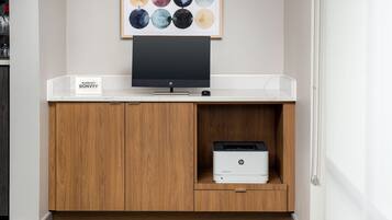 A clean, modern hotel room with a white console table, a flat-screen TV, and an HP printer.