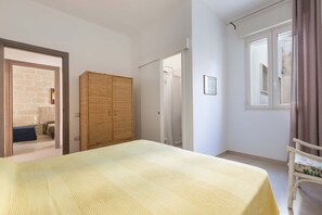 Un dormitorio con cama, armario, puerta que da a un baño y ventana con cortinas.