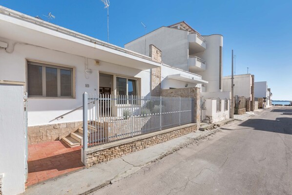 Un edificio residencial con fachada de piedra, una cerca metálica y cielo despejado.