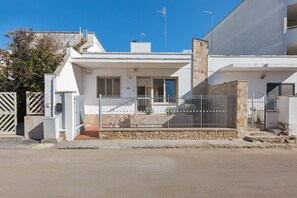Una casa moderna de dos pisos con fachada blanca, una chimenea de piedra y una cerca metálica.