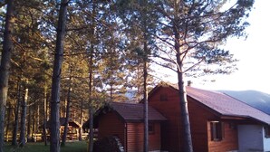 Une cabane rustique, dotée d’un toit en pente, entourée de grands pins et d’une clôture en bois.
