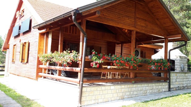 Une cabane en bois dotée d’un porche, de fondations en pierre et d’une cheminée en pierre.