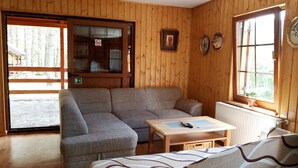 Une pièce chaleureuse avec des murs en bois, un canapé, une table avec une télécommande et une fenêtre agrémentée d’une plante.
