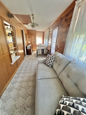 Un interior de cabaña acogedor, con un sofá, una cama, paredes de madera y un ventilador de techo.