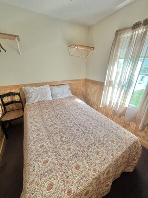 A bedroom with a large bed, a wooden headboard, a chair, a bedside table, and a window with curtains.