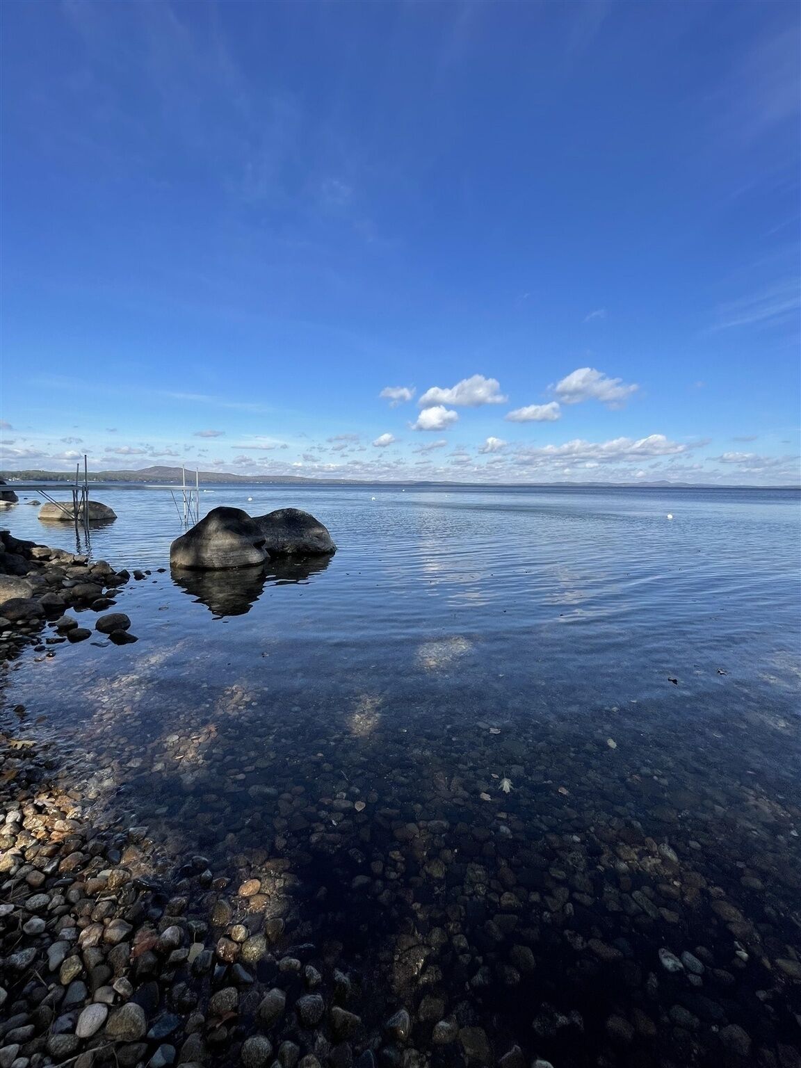 A clear lake with visible rocks and a dock extending into the water.