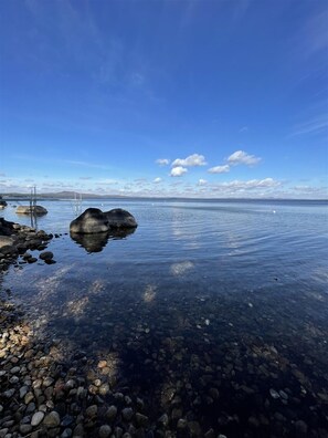Ein klarer See mit sichtbaren Felsen und einem Steg, der ins Wasser ragt.