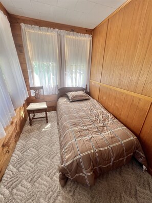 A bedroom with a wooden headboard, a bed with a patterned bedspread, a small wooden bench, and sheer curtains. - Hate To Leave It Limit 6 3 Bedroom Villa by RedAwning (Standish)