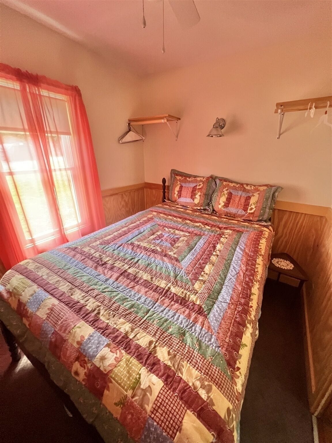 A bedroom with a large bed, a bedside table, a hanging lamp, and a window with curtains.