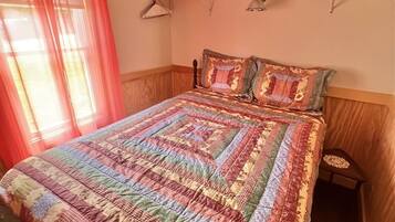 A bedroom with a large bed, a bedside table, a hanging lamp, and a window with curtains.