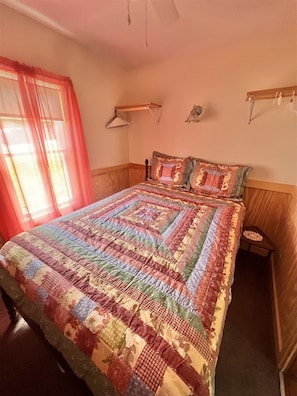 A bedroom with a large bed, a bedside table, a hanging lamp, and a window with curtains.