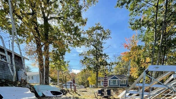 Uma área de estacionamento com calçamento de brita e guia amarela, rodeada por árvores e edifícios residenciais.