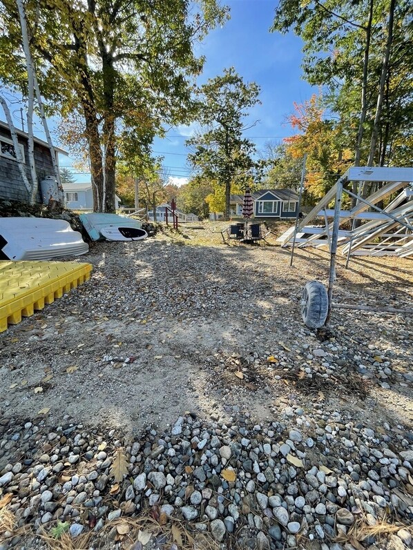 Ein Kiesparkplatz mit gelber Bordsteinkante, umgeben von Bäumen und Wohnhäusern.