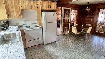 A kitchen with wooden cabinets, a white stove, a refrigerator, a sink, and a dining area with a table and chairs.