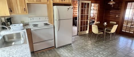 Una cocina con armarios de madera, una estufa blanca, un refrigerador, un lavamanos y una zona de comedor con mesa y sillas.