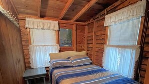 Um quarto de cabana de madeira aconchegante, com uma cama, uma mesa de cabeceira e duas janelas com cortinas.