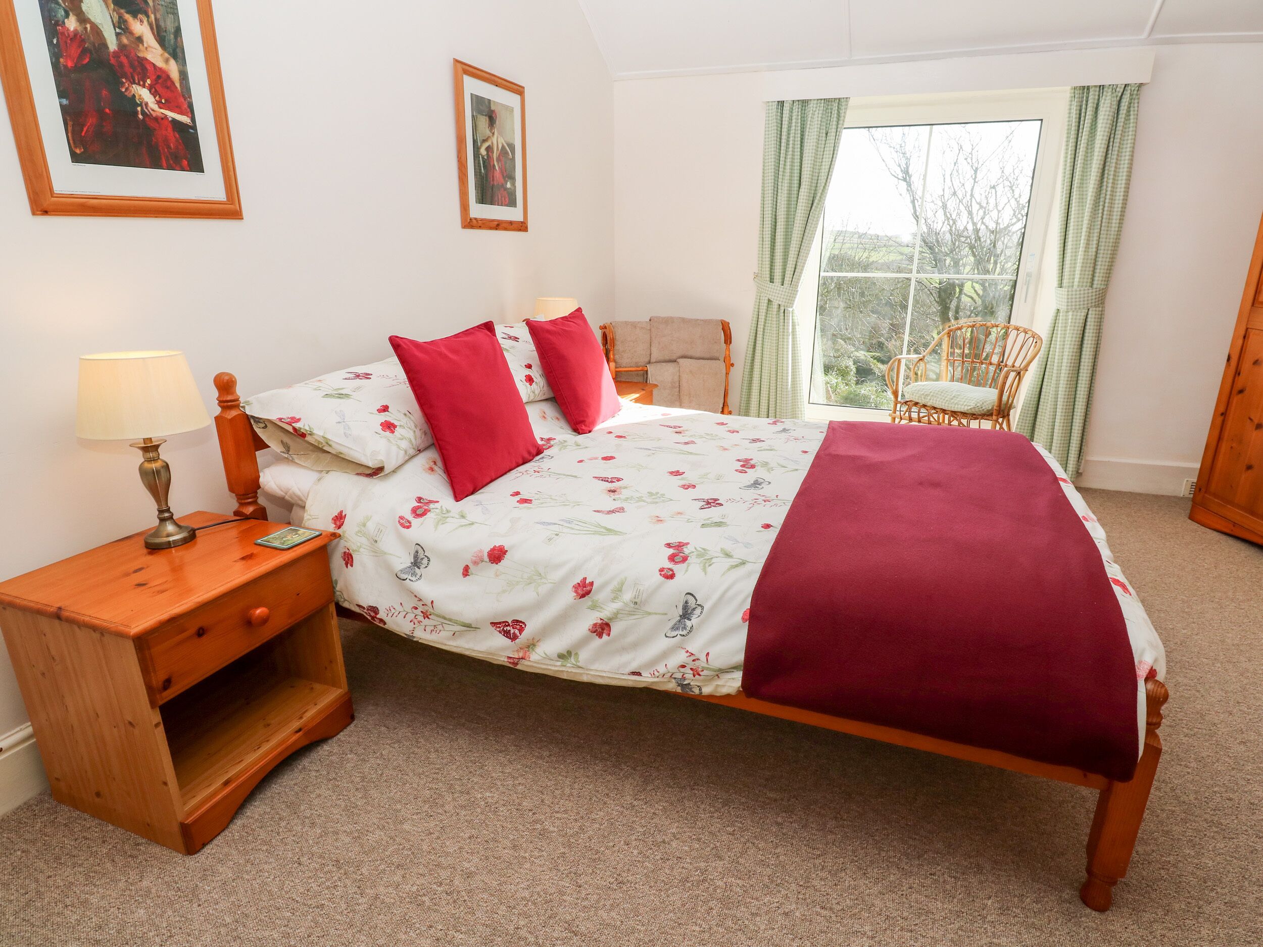 A bedroom with a bed, a nightstand, a lamp, a chair, and a window with curtains.