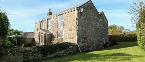 A stone house with a sloped roof, a satellite dish, and a small garden area.