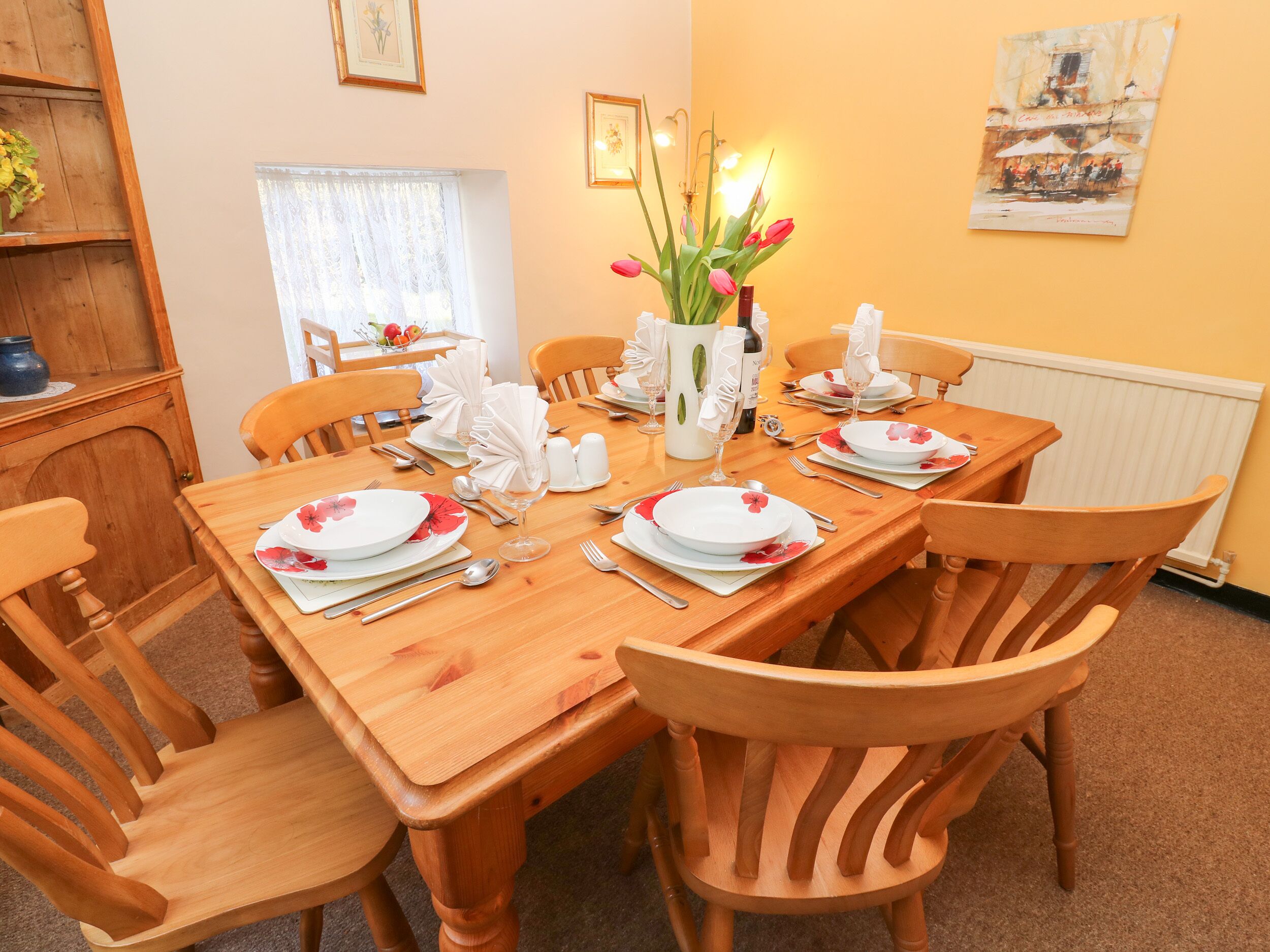 A dining area with a wooden table set for six, surrounded by wooden chairs.