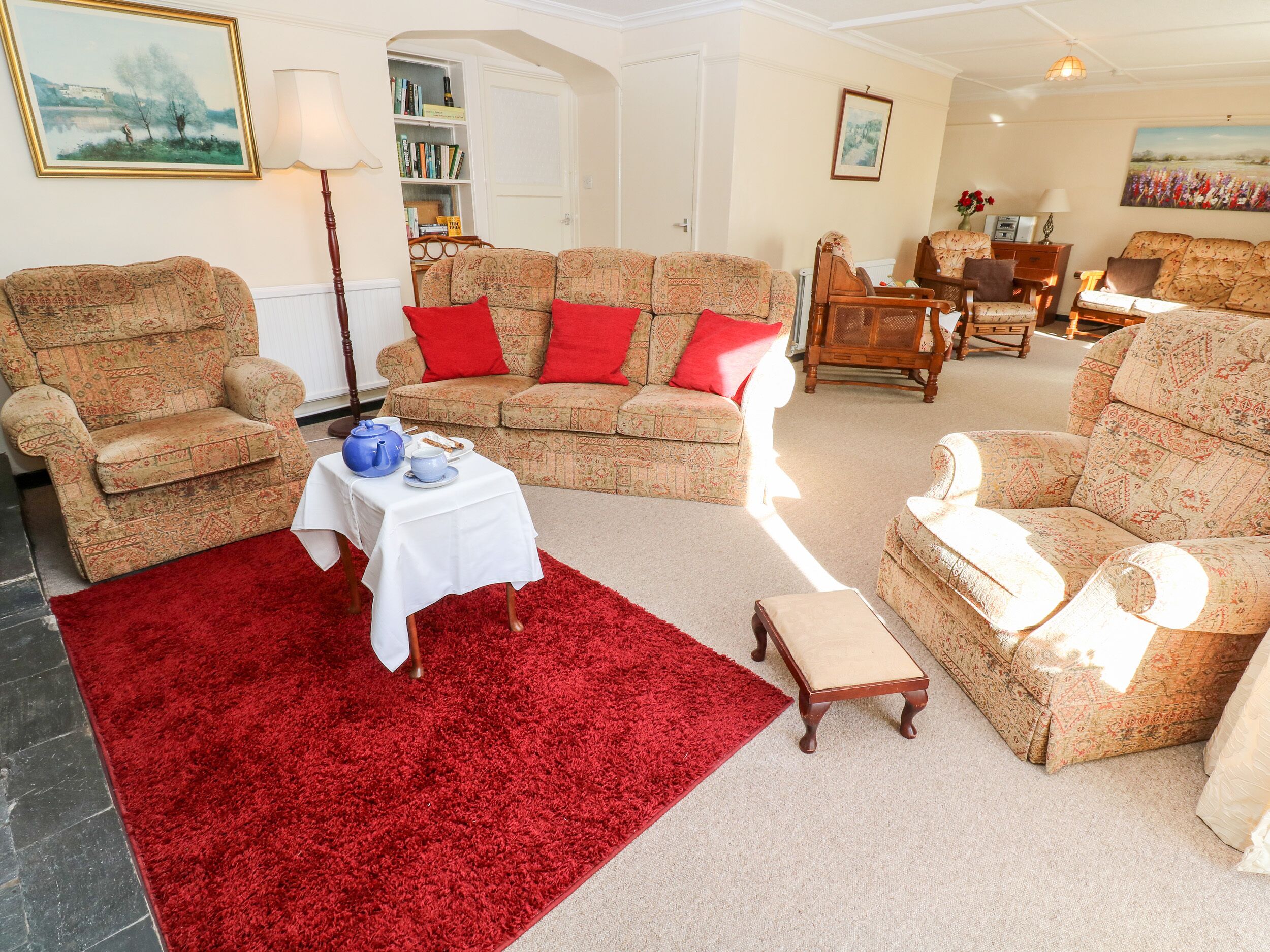 A cozy living room with patterned sofas, a red rug, and a small table with a teapot and cups.