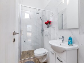 A modern bathroom with a glass shower enclosure, a toilet, a sink with a mirror, and a small vase with red flowers. - Villa Ketty (Fazana)