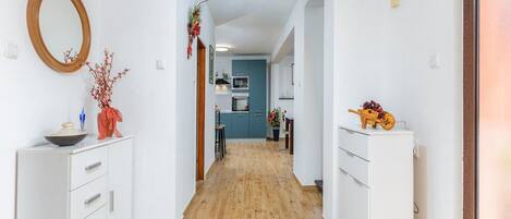 Un couloir avec des armoires blanches, un plancher en bois et, au fond, un espace cuisine.