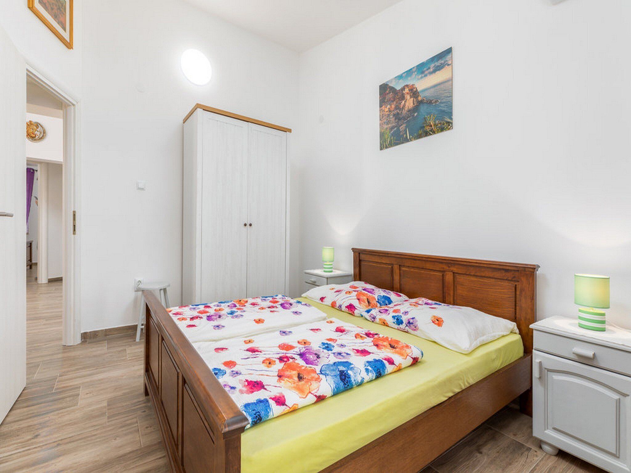 Un dormitorio con una cama de madera, un armario blanco, una mesita de noche con una lámpara y un cuadro en la pared.