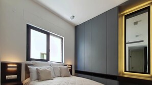 Un dormitorio moderno con una cama grande, mesitas de noche con lámparas, un espejo amplio y una ventana.