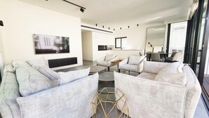 Una sala de estar moderna con un televisor de pantalla plana, dos sofás, una mesa de centro y una mesita auxiliar hexagonal.