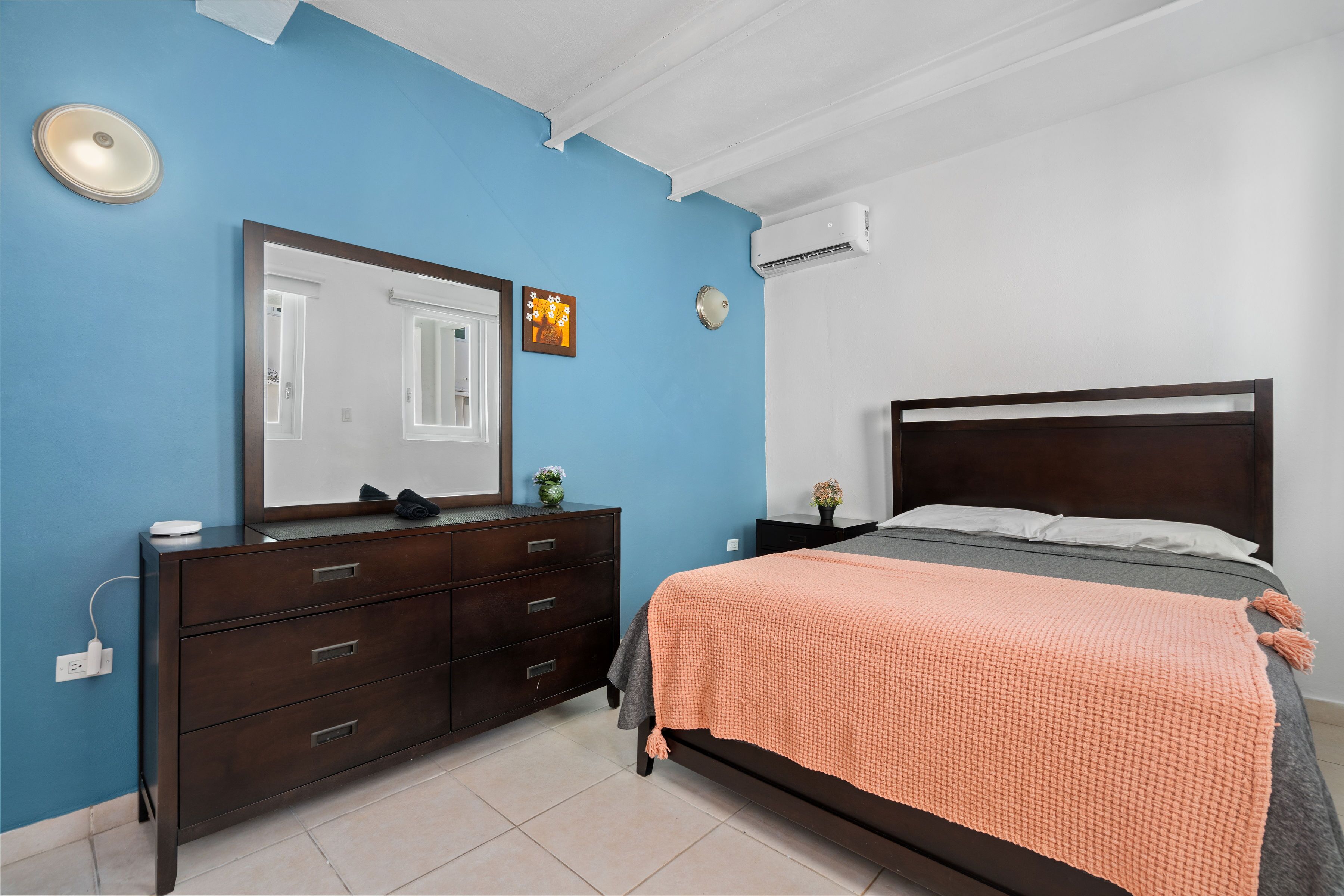 A bedroom with a dark wooden bed, a blue wall, a white ceiling, and a white air conditioning unit.