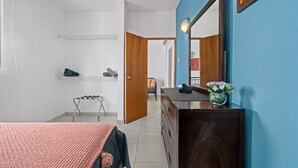 A bedroom with a bed, dresser, mirror, and a small table with a vase of flowers. - Puerto Rico Beachside Rental w Pool Otium Rentals (San Juan)