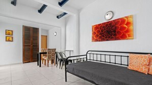 A bedroom with a bed, a dining area with chairs, a wooden door, and a large floral artwork on the wall. - Puerto Rico Beachside Rental w Pool Otium Rentals (San Juan)