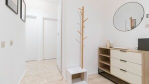 A hallway with a coat rack, a small white bench, a wooden cabinet with drawers, and a round mirror on the wall. - Italianway - Brianza 14 A (Milan)