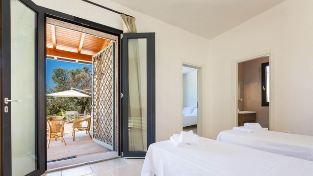 A hotel room with two beds, a sliding glass door leading to an outdoor area with wicker furniture and a table, and a small bathroom visible through the door. - 2081 Villa Crocilupo by Perle di Puglia (Gagliano del Capo)