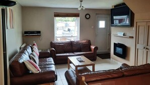 A living room with a brown leather sofa set, a wooden coffee table, and a flat-screen TV mounted on the wall. - Charming Two Bed Cottage Glan Gwna Holiday Park (Caernarfon)