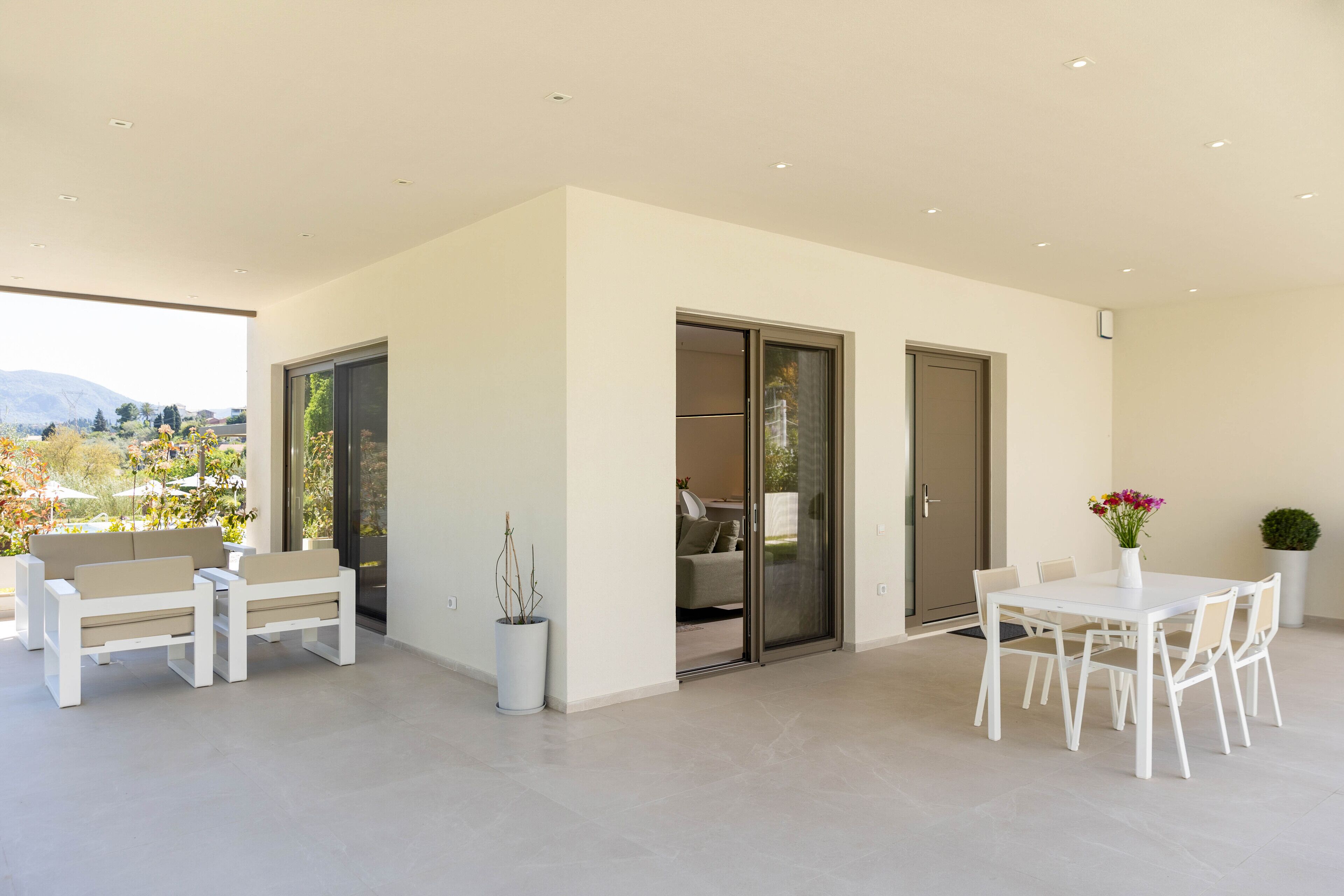 Een moderne patio met een witte tafel en stoelen, een potplant en een schuifdeur die leidt naar een binnenruimte.