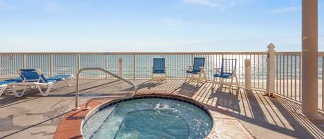 A pool area with a hot tub, lounge chairs, and a view of the ocean.
