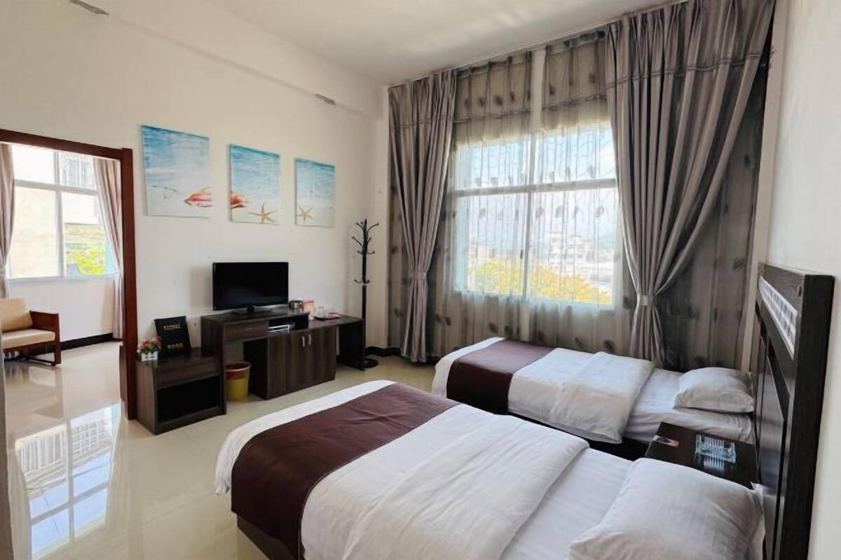 A hotel room with two beds, a TV, a desk, and a window with curtains.