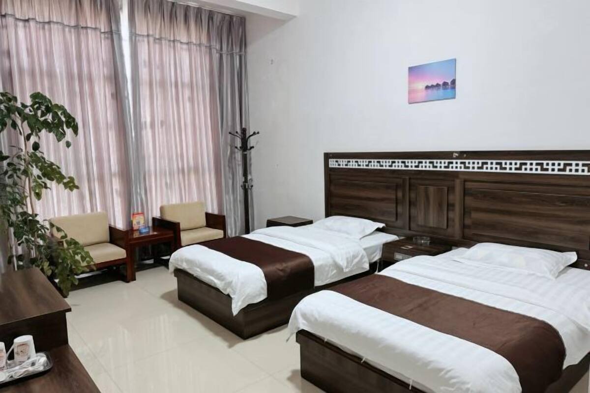A hotel room with two beds, a sofa, a coffee table, a plant, and a picture on the wall.