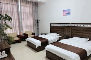 Habitación de hotel con dos camas, un escritorio, una silla y un amplio ventanal con cortinas.