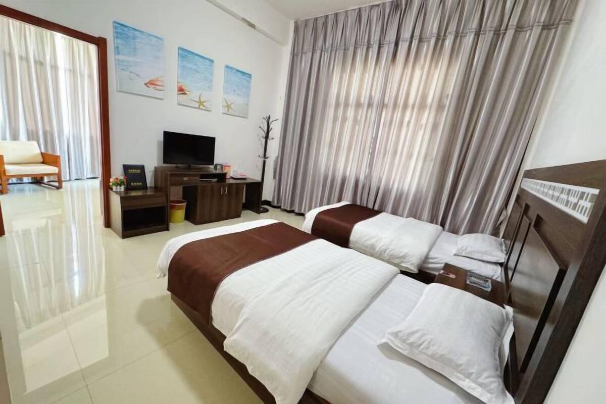 A hotel room with two beds, a TV, a desk, and curtains.