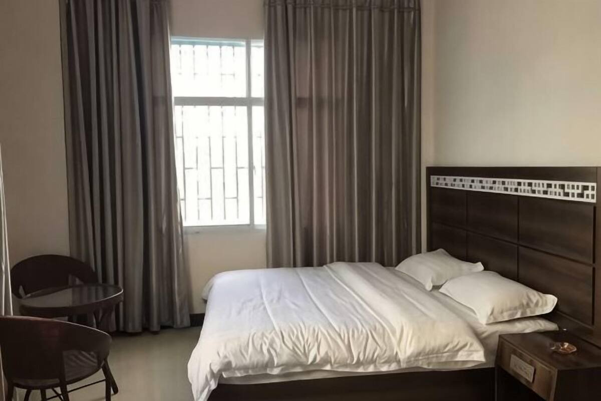 A hotel room with a bed, a nightstand, a chair, and a window with curtains.