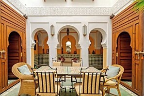 A traditional Moroccan interior with a central table and chairs, arches, and patterned tiles. - Family friendly, private Riad in the Heart of the Medina (Marrakech)