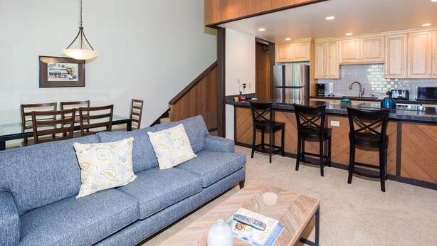 A modern kitchen with wooden cabinets, a stainless steel refrigerator, and a bar area with stools. - Three Kings 37 2 Bedroom Condo (Park City)