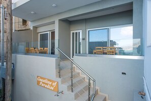 A modern building with a staircase leading to a balcony with glass railings and wooden chairs.